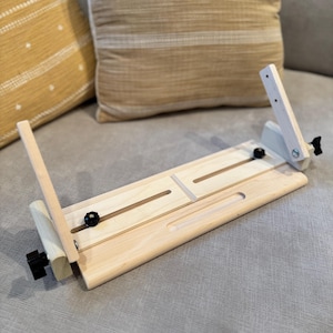Könnte beinhalten: Ein Laptopständer aus Holz mit verstellbaren Beinen und schwarzen Knöpfen. Der Ständer ist aus hellem Holz gefertigt und hat eine glatte Oberfläche.