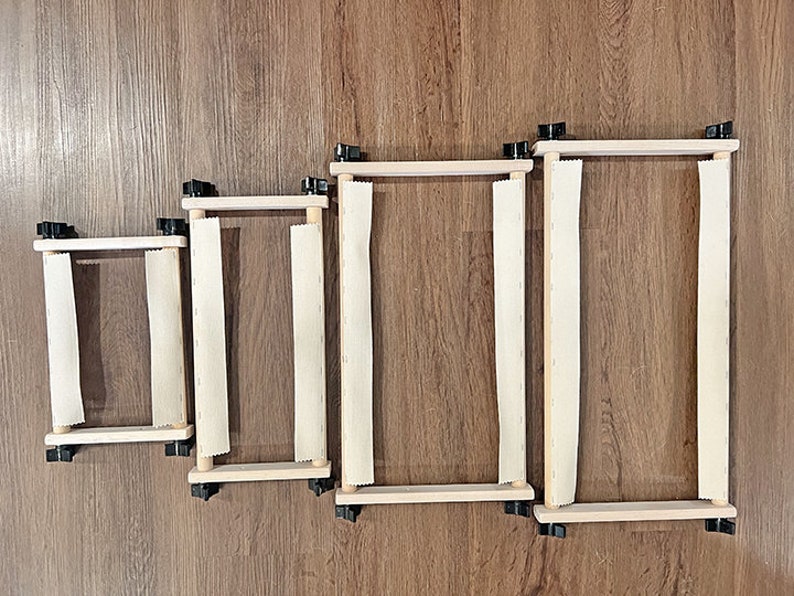 May include: Four wooden embroidery hoops of different sizes with white fabric stretched across them. The hoops are on a wooden floor.