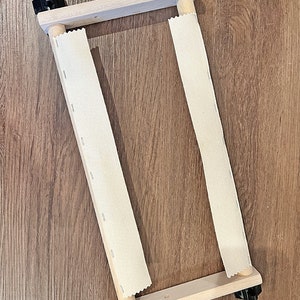 May include: A 13-inch wooden scroll frame with two white canvas rolls. The frame has black knobs on each corner.