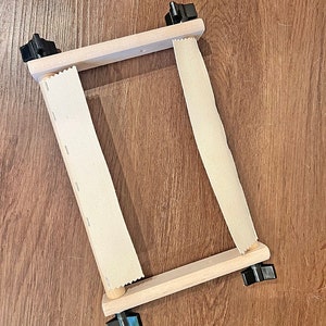 May include: A 9 inch wooden scroll frame with two white fabric strips and black knobs on each side.
