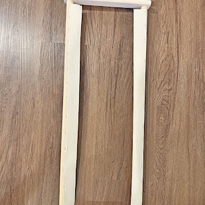 May include: A 24-inch wooden scroll frame with white fabric stretched across it. The frame is made of natural wood and has black metal clips at the top and bottom.
