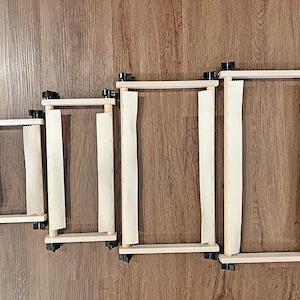 May include: Four wooden embroidery hoops of different sizes with white fabric stretched across them. The hoops are arranged in a row from smallest to largest.