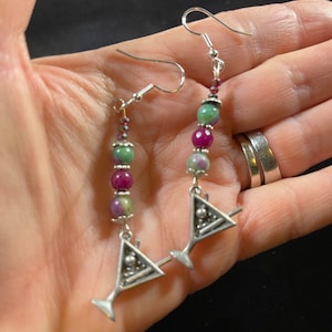 Peut inclure: Boucles d'oreilles pendantes en argent avec des perles de pierres précieuses vertes et roses et un charme en verre à martini argenté.