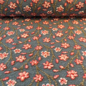 Könnte beinhalten: Nahaufnahme eines Stoffes mit einem sich wiederholenden Blumenmuster. Der Stoff hat eine gedämpfte teal Farbe, mit erhabenen, strukturierten Blumen in Rosa- und Weißtönen. Die Blumen sind durch braune Stiele verbunden.