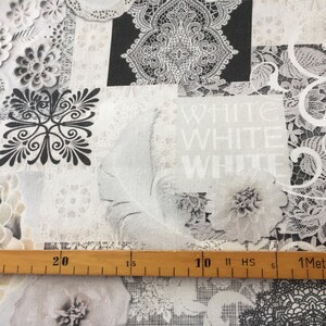 Könnte beinhalten: Weißer Stoff mit einem sich wiederholenden Muster aus schwarzer und weißer Spitze, Blumen und dem dreimal wiederholten Wort "WHITE". Am unteren Rand des Bildes befindet sich ein Holzlineal, das die Maße in Zentimetern anzeigt.