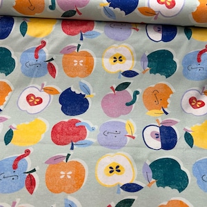 Könnte beinhalten: Hellgrüner Stoff mit einem sich wiederholenden Muster aus bunten Äpfeln. Die Äpfel sind in verschiedenen Farben gehalten, darunter Orange, Rot, Blau und Gelb, einige mit Bissspuren oder Würmern. Das Design ist skurril und verspielt.