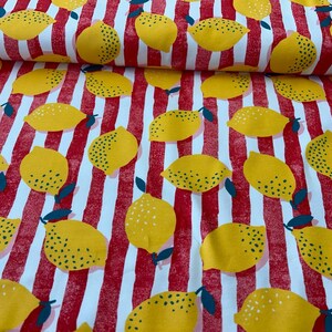 Könnte beinhalten: Weißer Stoff mit roten und weißen Streifen und einem gelben Zitronen-Druck. Die Zitronen sind über den Stoff verteilt und haben eine gesprenkelte Textur.