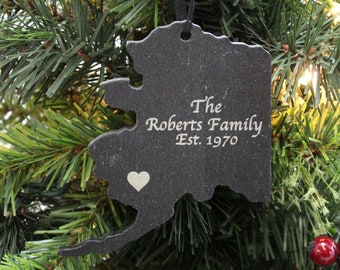 May include: A black slate Christmas ornament shaped like the state of Alaska. It is engraved with "The Roberts Family Est. 1970" and a small heart.