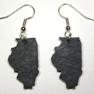 Op de afbeelding: Een paar oorbellen in de vorm van de staat Illinois, gemaakt van donkergrijze leisteen. De oorbellen hebben zilveren haken.