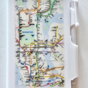 May include: A white pen with a Manhattan subway map design. The map features colorful lines representing subway routes, with street names and landmarks. The pen has a rectangular body and a white clip.