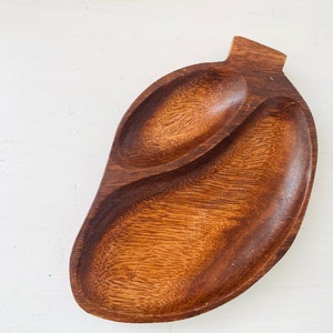May include: A wooden serving tray with two separate compartments. The tray is shaped like a heart and has a dark brown colour.