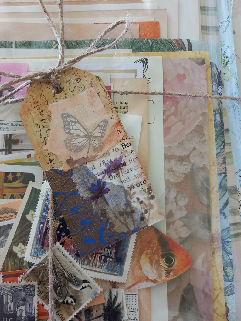 May include: A collection of assorted paper ephemera including vintage postage stamps, botanical prints, and map fragments, tied together with brown twine. A decorative tag features a butterfly illustration and a pressed blue flower on a textured background.