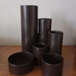 May include: A set of brown cylindrical and bowl-shaped objects of different sizes. The objects are displayed on a wooden surface. The tallest cylinder is about 20 cm high. The objects appear to be made of a solid, smooth material.