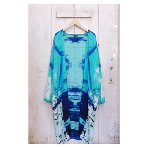 May include: A long, flowing blue and white kimono with an abstract print. The kimono is made of a lightweight fabric and has a relaxed fit.