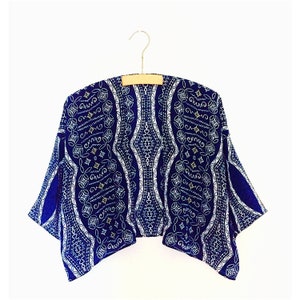 May include: A blue and white patterned kimono-style top with a geometric design. The top is hanging on a wooden hanger.