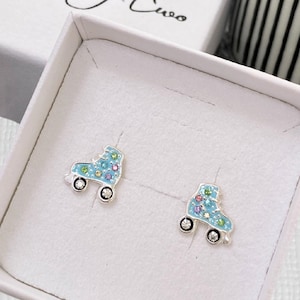 May include: A pair of silver roller skate earrings with blue enamel and colourful rhinestones. The earrings are in a white box with the text "kookytwo" on the bottom.