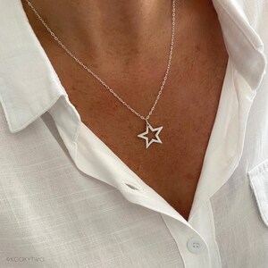 May include: A silver star pendant necklace. The open star design hangs from a delicate chain. The necklace is shown against a white button-down shirt.
