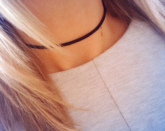 May include: A close-up of a person wearing a black choker necklace. The choker is made of a thin, black material and is worn around the neck.