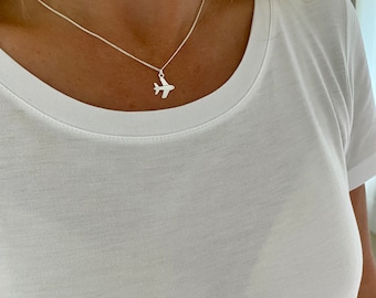 May include: A silver necklace with a small airplane pendant. The necklace is worn by a person wearing a white t-shirt.