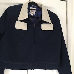 May include: A navy blue jacket with a white collar and two white pockets on the chest. The jacket has a zipper closure and a ribbed hem.