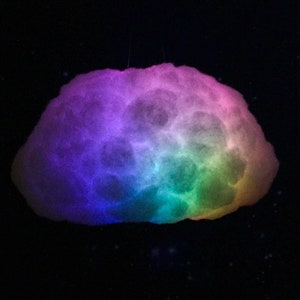 May include: A cloud-shaped light fixture with a gradient of colors, including purple, blue, green, and yellow. The fixture is suspended against a black background, creating a celestial effect. The light appears to be soft and diffused.