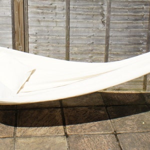 May include: A white hammock hanging between two wooden posts. The hammock is made of a soft, woven fabric and is perfect for relaxing outdoors.