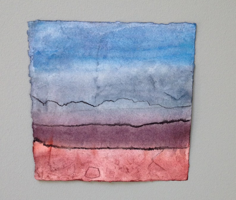 May include: A watercolour painting with a colour gradient. The top is blue, fading to grey, then purple, and finally red at the bottom. The paper edges are rough and uneven.