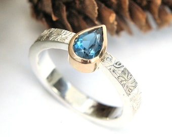 Anillo solitario de topacio azul Londres en forma de pera, en plata y oro, con banda texturizada en espiral. HECHO A PEDIDO.