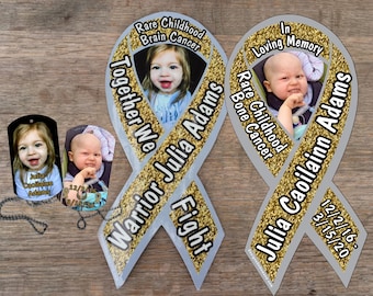 May include: Two gold ribbon magnets with a photo of a young girl and the text "Together We Warrior Julia Adams Fight" and "In Loving Memory Julia Caoilainn Adams" and dates.  The magnets are on a wood background.