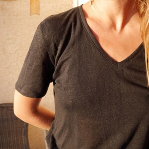 Könnte beinhalten: Ein schwarzes V-Ausschnitt-T-Shirt aus leichtem Stoff. Das Shirt ist locker geschnitten und hat eine lockere Silhouette.