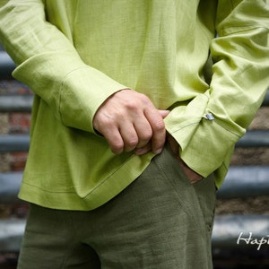 May include: A light green linen shirt with long sleeves and a button-down collar. The shirt is tucked into olive green pants.