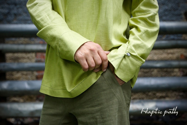 May include: A light green linen shirt with long sleeves and a button-down collar. The shirt is tucked into olive green pants.