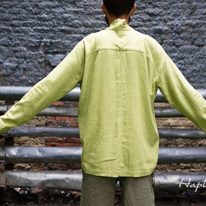 May include: A light green long-sleeved shirt with a high collar and a single button closure at the neck. The shirt is made of a lightweight fabric and has a relaxed fit.