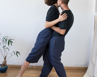 May include: Two people are embracing, one person is holding the other person from behind. Both people are wearing dark blue pants and black shirts.