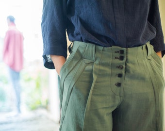 May include: A pair of green pants with a dark blue shirt. The pants have a button fly and multiple buttons down the front.