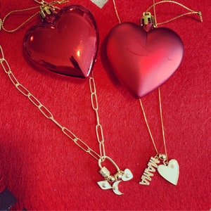 Pu&ograve; includere: Due ornamenti rossi a forma di cuore con catene e ciondoli dorati. Un ciondolo &egrave; un cuore con la parola "Mamma" su di esso. Gli ornamenti sono su uno sfondo di feltro rosso.