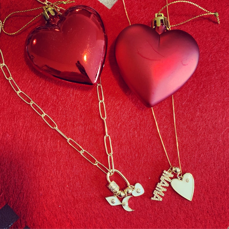 Pu&ograve; includere: Due ornamenti rossi a forma di cuore con catene e ciondoli dorati. Un ciondolo &egrave; un cuore con la parola "Mamma" su di esso. Gli ornamenti sono su uno sfondo di feltro rosso.