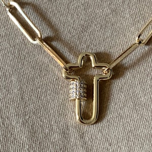 May include: A gold chain necklace with a cross-shaped clasp. The clasp is decorated with small clear rhinestones.