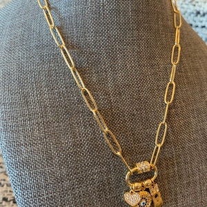 Pu&ograve; includere: Una collana a catena dorata con un ciondolo a forma di cuore, un occhio malvagio e un piccolo ciondolo con una lettera. La catena &egrave; in metallo dorato e ha una chiusura a moschettone.