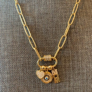 Pu&ograve; includere: Una collana a catena dorata con un ciondolo che presenta un occhio blu malocchio, un cuore e le lettere "MOM".