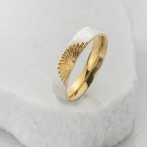 Peut inclure: Une bague en or et argent avec un motif de soleil. La bague présente un extérieur en argent brossé et un intérieur en or poli. Le motif de soleil est gravé dans la bande d'argent.