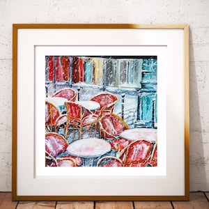 Könnte beinhalten: Gerahmter Kunstdruck einer Pariser Cafészene. Das Gemälde zeigt rote Stühle und weiße Tische im Schnee. Der Hintergrund zeigt farbenfrohe Gebäude und eine blaue Säule. Das Kunstwerk ist in einem goldfarbenen Holzrahmen gerahmt.