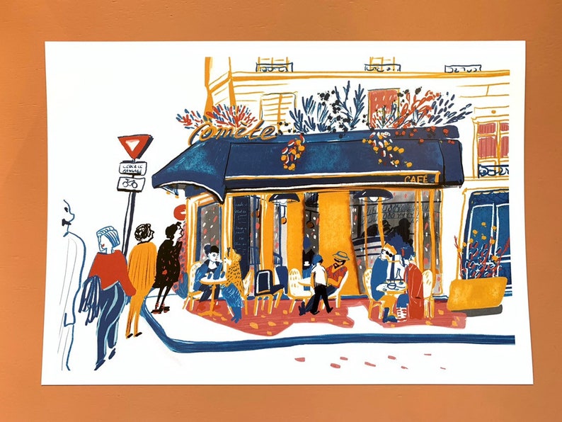 Puede incluir: Una ilustraci&oacute;n pintada a mano de un caf&eacute; parisino con un toldo azul y la palabra "Comte" escrita en &eacute;l. El caf&eacute; est&aacute; lleno de gente sentada en mesas y disfrutando del caf&eacute;. La ilustraci&oacute;n est&aacute; hecha en un estilo colorido y caprichoso.
