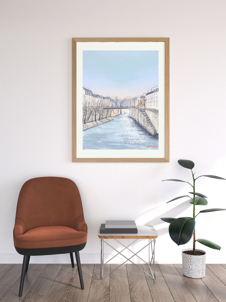 Peut inclure: Une peinture &agrave; l'aquarelle encadr&eacute;e d'un paysage urbain parisien avec une rivi&egrave;re qui coule au centre. Les b&acirc;timents sont blancs avec des toits bruns et des arbres bordent les rives de la rivi&egrave;re.