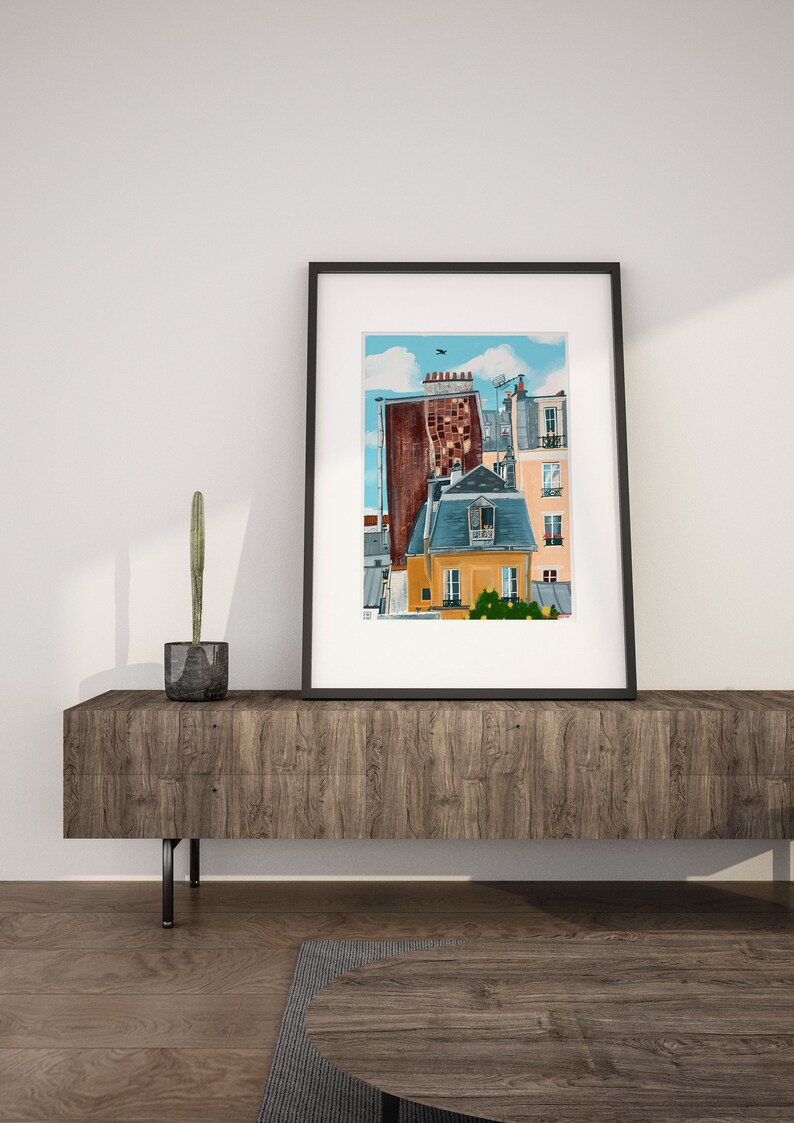 May include: A framed illustration of a Parisian cityscape with a blue sky and white clouds. The illustration features a brown building with a yellow building in front of it. The yellow building has a window with a balcony and a small tree in front of it.