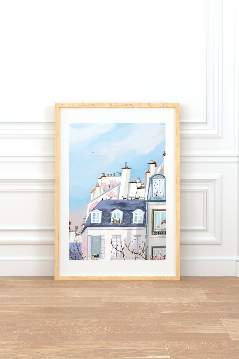 May include: A framed illustration of a Parisian cityscape with white buildings, blue roofs, and pink flowers. The illustration is painted in a watercolor style and features a light blue sky with white clouds.