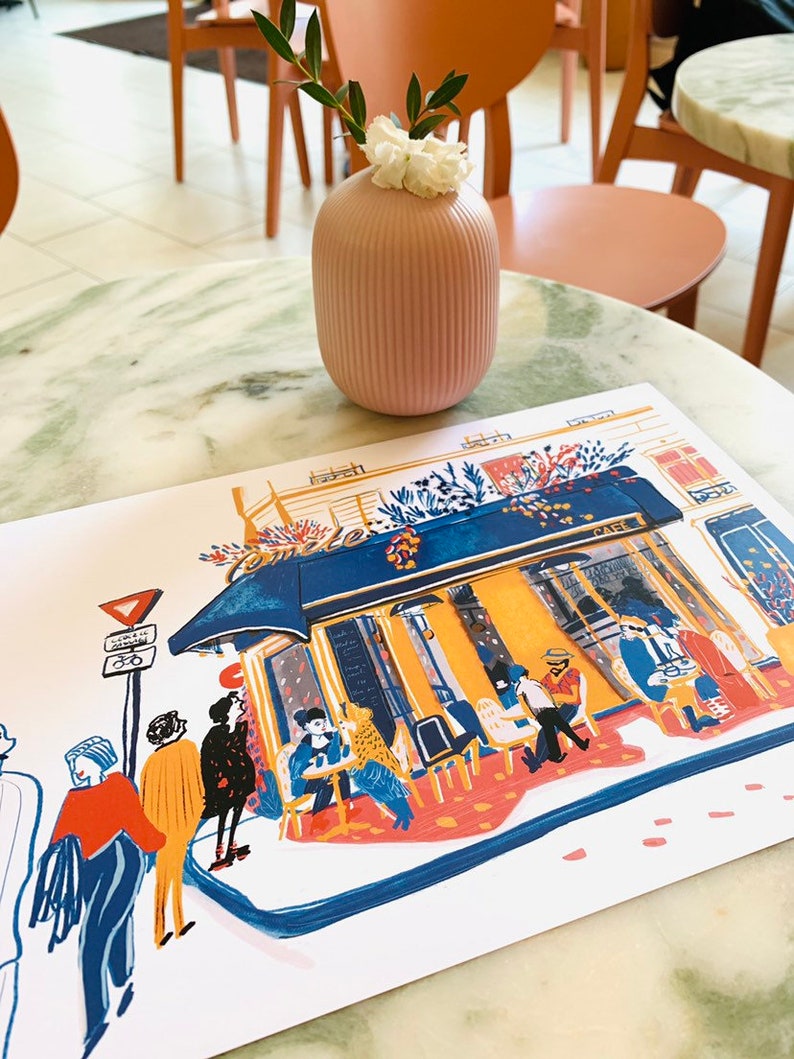Puede incluir: Una ilustraci&oacute;n colorida de un caf&eacute; parisino con gente sentada afuera. La ilustraci&oacute;n est&aacute; impresa en una tarjeta blanca y est&aacute; sobre una mesa de m&aacute;rmol con un jarr&oacute;n rosa con flores blancas.