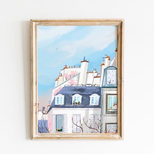 May include: A framed illustration of a Parisian cityscape with white buildings, blue roofs, and pink flowers. The illustration features a blue sky with white clouds and a glimpse of a person looking out a window.