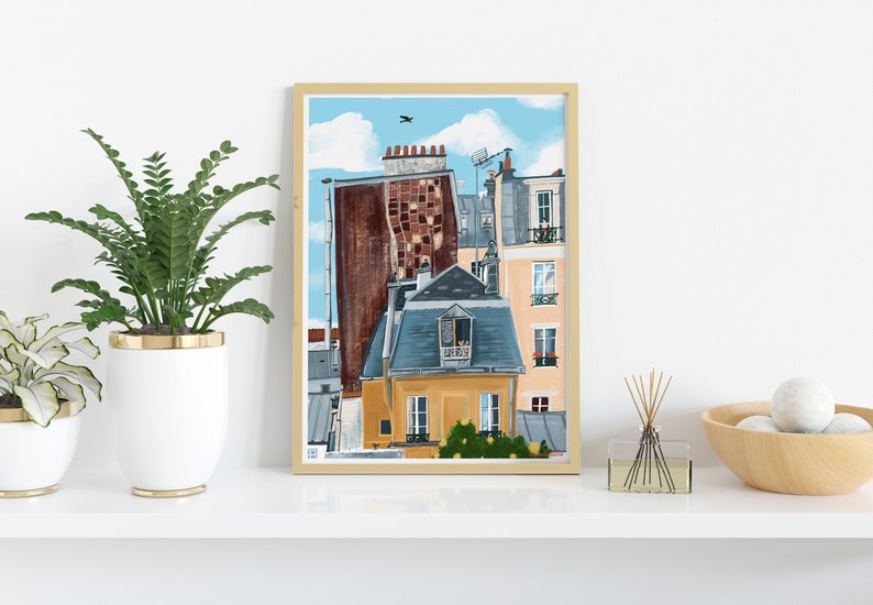 May include: A framed illustration of a Parisian cityscape with a blue sky, white clouds, and a bird flying overhead. The buildings are painted in shades of yellow, orange, brown, and grey. The illustration is framed in a light wood frame.