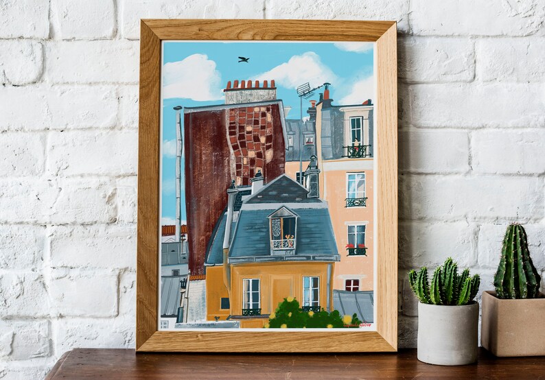 May include: A framed painting depicting a colourful cityscape with multiple buildings. The buildings are painted in shades of brown, yellow, blue, and grey. The painting has a blue sky with white clouds and a small bird flying in the sky.